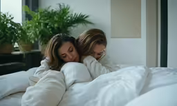 two women in bed embracing each other, hugging