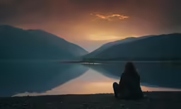 a woman sitting on the ground watching the sun set