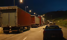 a car driving down a road with multiple semi trucks,trucks on a road with cars on both sides