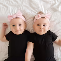 two babies lay on a bed with white sheets