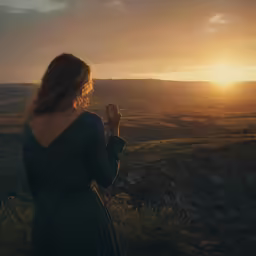 a woman standing in the mountains with the sun going down