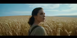 a woman standing in a wheatfield looking into the distance