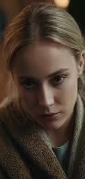 a young blonde woman wearing a brown coat looking to her left