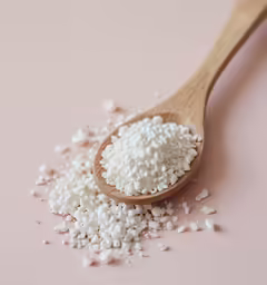 sprinkled seeds in wooden spoon on pink surface