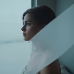 a young woman wearing a white dress looks out a window