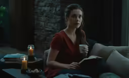 a woman sitting on top of a couch next to a cup