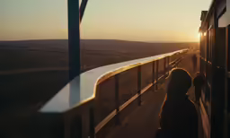 people are standing outside on the side of the train at sunset