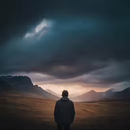 a person is staring towards mountains with clouds overhead