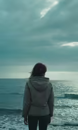 woman on beach looking out to the ocean during cloudy day