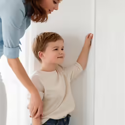 a little boy standing by a wall and looking at his mom