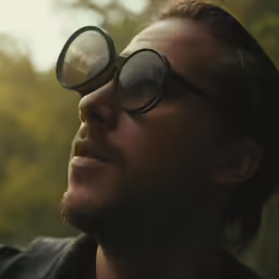 the man wearing round glasses is looking up