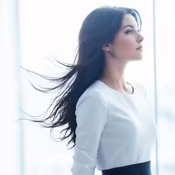 a woman in a white shirt and black pants with her hair flying in the wind