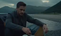 a man sits by the water with a motorcycle