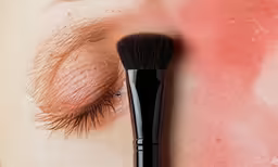 closeup of a womans left eye with red pigment makeup brush