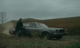 a person sitting on the hood of an older car