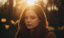 a young woman stands in a sunlit forest