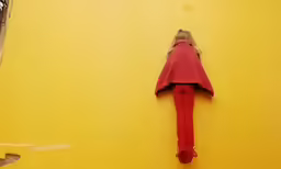 a woman with a red jacket is laying on a yellow wall