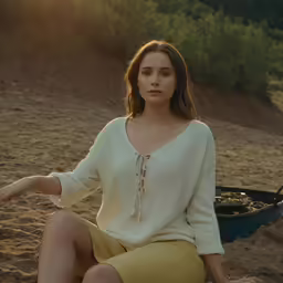 a woman wearing a cream sweater sits on a beach