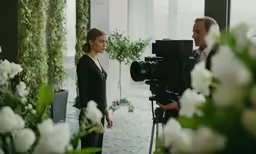 a man and woman standing together, each holding a camera, and facing the camera