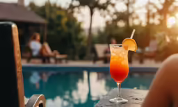 the person is sitting by the pool drinking orange juice