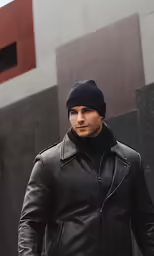 man wearing black leather jacket and hat standing in front of building