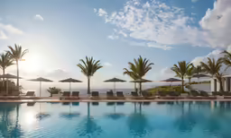 several umbrellas are over an outdoor pool near a view of the ocean