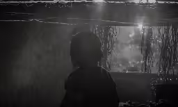 a silhouette of a man standing in the rain in front of trees