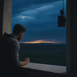 man looking out window at dusk over the valley