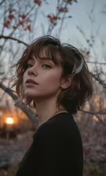 a woman standing next to trees and sunset in the background