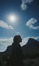 a woman standing in front of the sun and clouds
