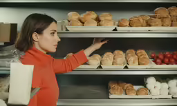a woman in an orange sweater is looking at the shelves full of breads