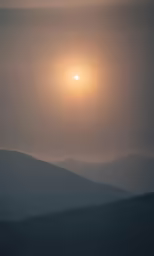 the sun setting over some hills in the distance