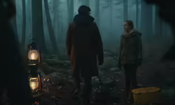 two people standing in a dark wooded area with lights on