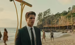 a man in a suit and tie on the beach near some people