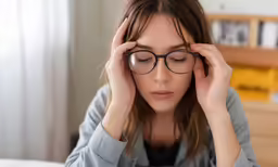 a girl wearing glasses holds her hands over their temples