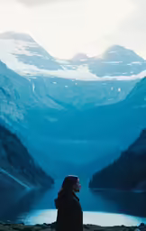 a person with a black coat standing by a lake