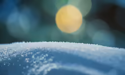 a close up of a snowy surface with blue boke of light in the background