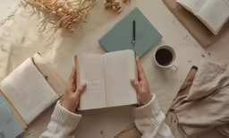 a person in white sweater writing on top of an open book