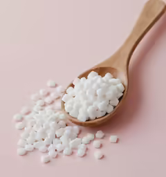 spoon full of white sugar sitting on top of a pink surface