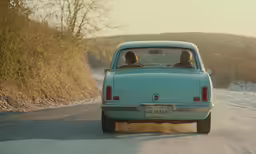 a man sitting in a small blue car on a snowy road