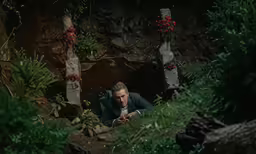 a man in green jacket crouches down next to some plants