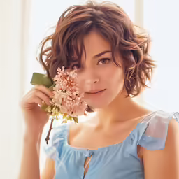 a women holding a flower standing next to a window