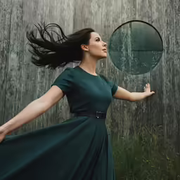 a woman holding out her arms in front of a large circular mirror