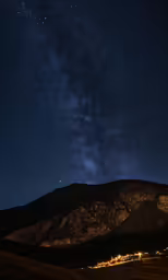 a mountain side with some light pollution underneath it and stars