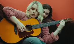 there are two beautiful women sitting together and playing the guitar