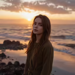a woman in green shirt standing on beach at sunset