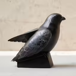 a small metal bird sitting on top of a wooden base