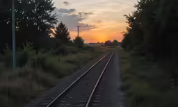 sunset in the distance on train tracks near grassy area