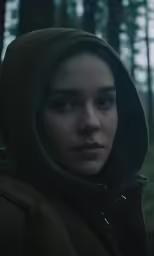 a girl is looking at the camera while standing in a forest