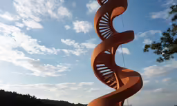 a spiral shaped sculpture is in front of trees